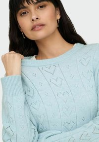 Pull tricoté bleu clair avec motifs en forme de cœur, poignets et encolure côtelés. Présente une coupe décontractée et des détails texturés sur l'ensemble.