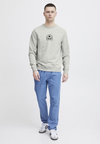 Lys grå hettegenser med rund hals og svart trykkdesign på brystet, kombinert med blå denimbukser og svart-hvite joggesko.