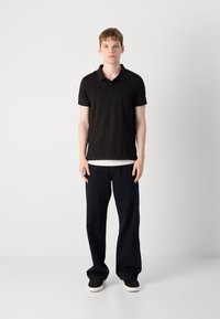 Čierna polokošeľa s krátkymi rukávmi, golierom, skombinovaná s tmavomodrými širokými džínami a čiernymi teniskami. Jednoduchý, neformálny outfit bez vzorov.