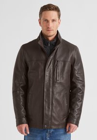 Braune Lederjacke mit Stehkragen, einer Reißverschlusstasche vorne und seitlichen Taschen. Glatte Textur und taillierte Passform, kombiniert mit lässigen Jeans.