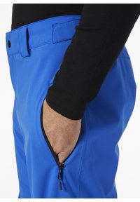 Modré kalhoty s kapsou na zip, vyrobené z hladkého, lehkého materiálu. Pas má poutek na opasek a zapínání na knoflík.