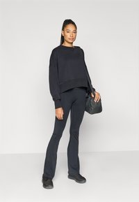 Sort cropped sweatshirt med oversize ærmer, kombineret med sorte flared leggings og sorte sneakers. Holder en sort skuldertaske.