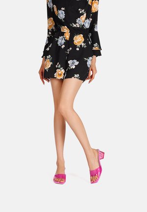Sandali con tacco trasparente rosa, dal design open-toe e con tacco quadrato. Il materiale ha una finitura lucida, che contrasta con la tuta floreale.