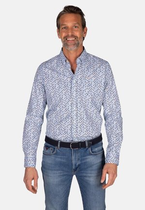 Lichtblauwe langärmige shirt met een meerkleurig stippenpatroon, met knoopsluiting aan de kraag, gecombineerd met blauwe jeans en een zwarte riem.