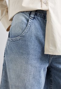 Vaqueros de mezclilla azul claro con un corte relajado, que cuentan con un gran bolsillo delantero, una cinturilla estructurada y una textura suave.