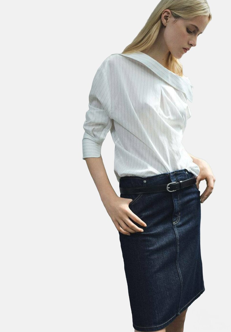 Witte blouse met pinstripes, off-shoulder, met lange mouwen, gecombineerd met een donkere denim kokerrok, voorzien van een voorzak en een zwarte riem.