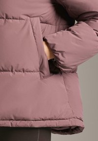 Pikowana lawendowa kurtka o luźnym kroju, z boczną kieszenią i elastycznymi mankietami dla ciepła i wygody. Miękka, gładka w dotyku.