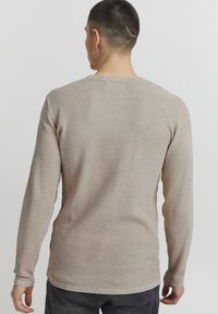 Long-sleeve beige thermal shirt with a textured, ribbed fabric, a crew neckline, and a straight hemline, shown from the back.