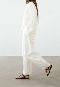 White linen long-sleeve shirt and wide-leg pants, with a relaxed fit; paired with minimal black sandals featuring a strap design.