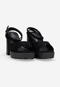 Sandalias de plataforma de ante negro con un tacón grueso, punta abierta y correas cruzadas en el tobillo. Suela texturizada con un forro interior suave.