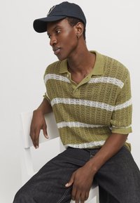 Zelený pletený polo shirt s bílými pruhy, krátkými rukávy a límcem. V kombinaci s tmavými džíny a námořnickou čepicí.