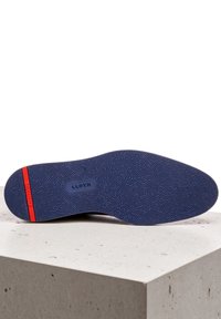 Semelle de chaussure avec une surface en caoutchouc bleu texturé et une bande d'accent rouge ; le nom de la marque "LLOYD" est embossé sur le côté.
