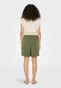 Hellbeige strukturierte Bluse mit kurzen Ärmeln und einem gerippten Saum, kombiniert mit grünen, plisseeartigen Shorts. Schlichtes Design mit einer lockeren Silhouette.