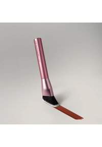 Pinceau de maquillage biseauté avec un manche rose portant l'inscription "real techniques RT 4568" appliquant un trait de couleur brun rougeâtre sur une surface claire.