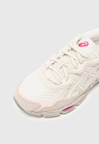 Ljusfärgad löparsko med övre av mesh, mockadetaljer och vadderad krage. Detaljer inkluderar en rosa logotyp och mönstrad yttersula.