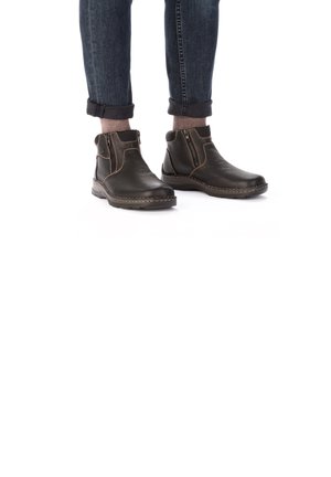 Schwarze Leder-Stiefeletten mit strukturierter Oberfläche, ausgestattet mit kontrastierenden braunen Nähten und seitlichen Reißverschlüssen, kombiniert mit umgeschlagenen Denim-Jeans.