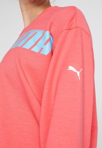 Korálová mikina, s modrým logem PUMA přes hrudník a malým bílým logem na rukávu. Měkká, strukturovaná látka.