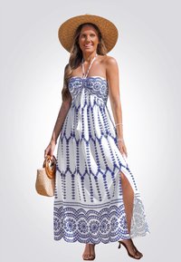 Vestido maxi de tela blanca con bordado azul en patrón, diseño sin tirantes y abertura alta. Llevado con un sombrero de paja de ala ancha.