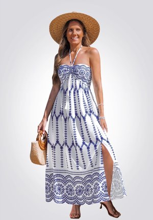 Vestido maxi de tela blanca con bordado azul en patrón, diseño sin tirantes y abertura alta. Llevado con un sombrero de paja de ala ancha.