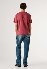 Camiseta de algodón de color rojo desgastado de manga corta con cuello redondo. Combinada con unos jeans de denim azul de talle alto y zapatos negros.