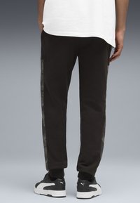 Pantaloni de trening negri cu picior tapered, având un panou lateral texturat și margini cusute, asortați cu adidași negri și albi.