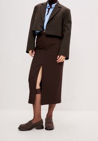 Blazer court marron sur une chemise bleue, associé à une jupe marron longue aux genoux avec une fente à l'avant. Des mocassins marron complètent la tenue.