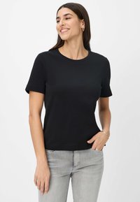 Schwarzes Kurzarm-T-Shirt mit Rundhalsausschnitt, aus glattem Stoff gefertigt. Getragen mit hellgrauen Jeans, die einen bequemen Sitz bieten.
