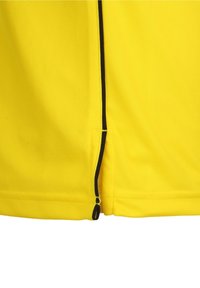 Žlutý atletický dres s texturovanou síťovinou. Obsahuje černý zip a akcentovou výšivku po stranách.