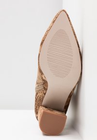 Semelle de chaussure avec motif peau de serpent beige et marron, bout pointu, talon bloc, et semelle en caoutchouc texturée pour une meilleure adhérence.