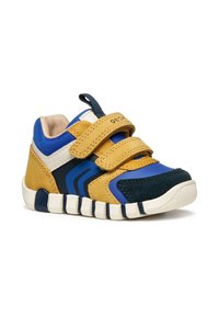 Zapatilla deportiva con paneles amarillos, azules y marinos. Incluye un cierre de tira de velcro, suela de goma texturizada y acentos cosidos.