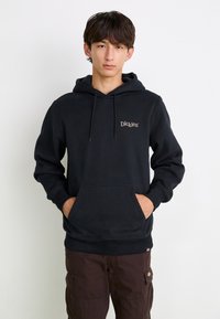 Black hoodie made of cotton blend, featuring a front pocket, drawstring hood, and a small embroidered logo. Worn with brown cargo pants.