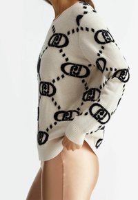 Strickpullover in Creme mit schwarzem Logomuster. Verfügt über gerippte Bündchen und Saum. Weicher, strukturierter Stoff. Design beinhaltet Ketten und Punkte.