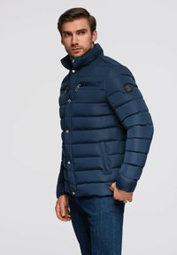 Marinblå puffjacka med quiltat mönster, hög krage, dragkedjefickor på bröstet, knappstängningar och sidofickor, tillverkad av vattentåligt material.