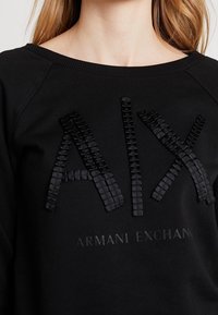 Felpa nera con logo "AIX" testurizzato e "ARMANI EXCHANGE" in un delicato finish opaco. Collo a giro e maniche raglan.