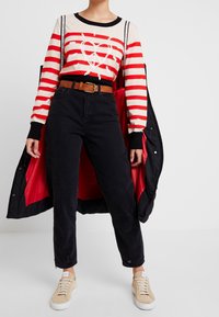 Červeno-bílý pruhovaný svetr s motivem srdce, černé džíny s vysokým pasem, hnědý pásek a béžové tenisky; černý kabát s červeným podšívkou.