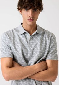 Polo gri cu un model repetitiv, cu mâneci scurte și guler de un gri deschis, având nasturi la gât. Textură de țesătură moale.