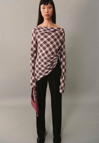 Langärmliges karierter Oberteil in Burgunder- und Cremetönen mit Drapierungsdetails, kombiniert mit schwarzen Hosen und einer kleinen rosa Handtasche.