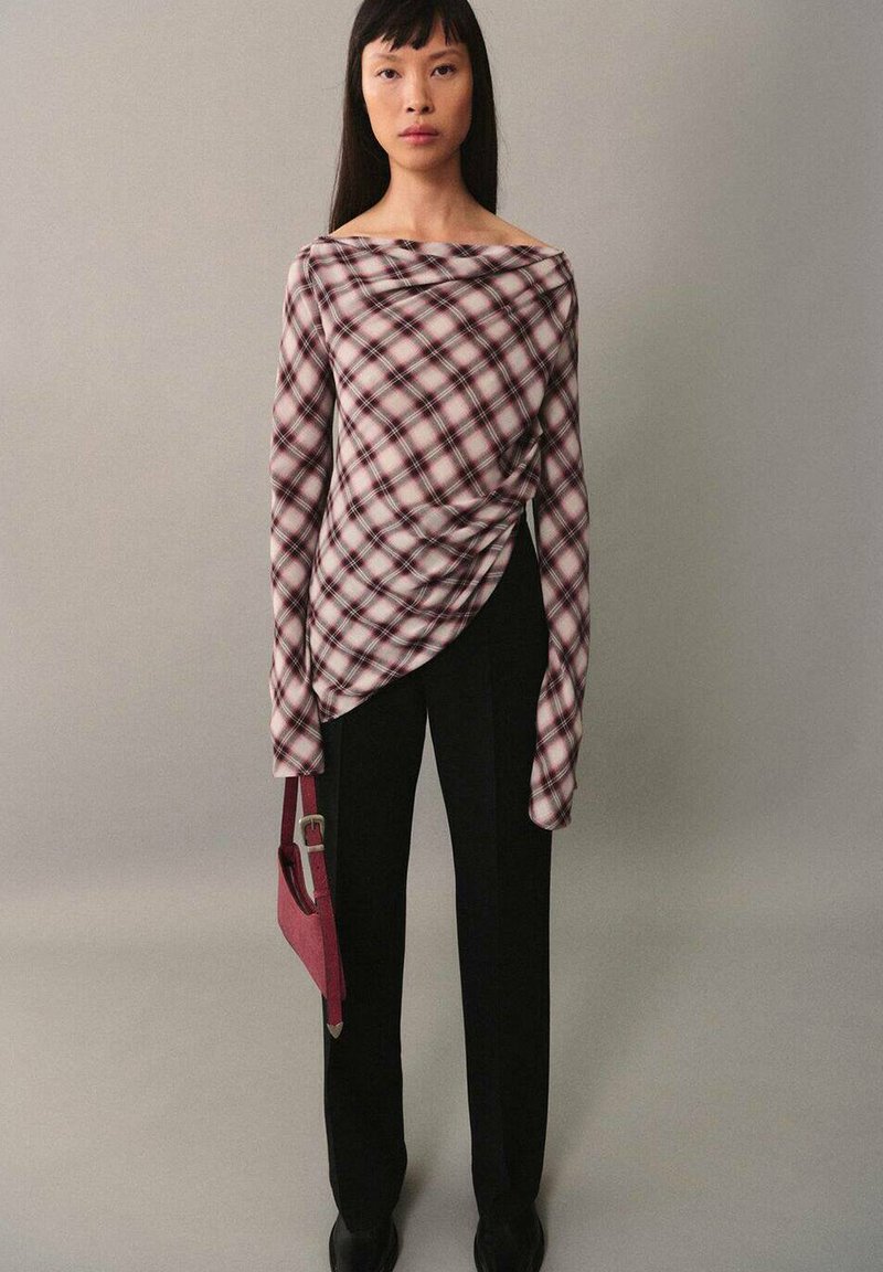 Langärmliges karierter Oberteil in Burgunder- und Cremetönen mit Drapierungsdetails, kombiniert mit schwarzen Hosen und einer kleinen rosa Handtasche.