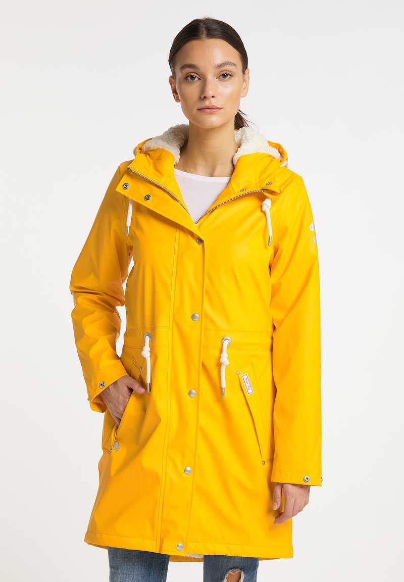 Geel waterdicht regenjack met een witte bont gevoerde capuchon, trekkoord aanpassingen, drukknoopsluitingen en twee voork pocket.