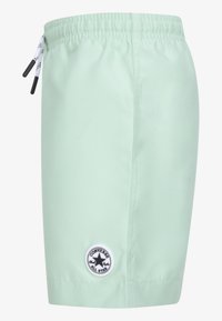 Heledad rohelised ujumispüksid, millel on elastne vöökoht, nöörpael ja ümmargune must-valge Converse logo plaastril küljel.