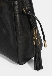 Zwarte gestructureerde leren tas met een gouden metalen accent en een kwastje. De vorm is hoekig met een stevige basis en zachte randen.