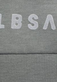Fodera di felpa grigia con grandi lettere bianche e pelose. La trama mostra un maglione liscio con orlo inferiore a costine.
