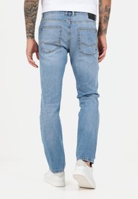 Jasnoniebieskie dżinsy o slim fit, z klasycznym pięciopocketowym wzorem i kontrastującymi przeszyciami, noszone z białymi sneakersami.