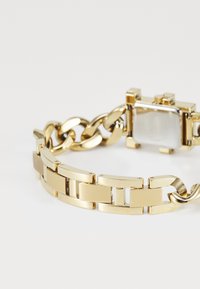 Bracciale in metallo color oro a maglie con quadrante rettangolare e cassa in madreperla su sfondo bianco.