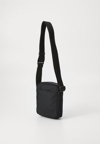 Borsa a spalla nera in tessuto con superficie texturizzata, tracolla regolabile e tasca frontale con zip. Forma rettangolare compatta.