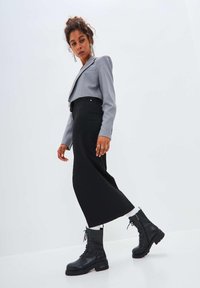 Falda negra y blazer gris corto con un solo bolsillo en el pecho. La modelo lleva botas de combate negras con cordones y anillos, con un peinado texturizado.