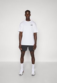 Valge puuvillane T-särk lühikeste varrukatega, millel on must Puma logo. Kombineeritud mustade lühikesed püksid ja valged spordijalanõud mustade aktsentidega.