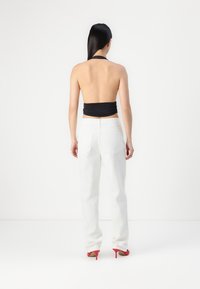 Fekete nyakpántos crop top, amelyet laza, magas derekú fehér farmerral és piros magassarkú cipővel párosítottak. Zökkenőmentes textúrák és minimalista dizájn.