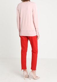 Jasnoróżowy sweter z dzianiny z ribbowym dołem, w zestawieniu z czerwonymi spodniami typu tapered z postrzępionymi mankietami i cielistymi szpilkami.