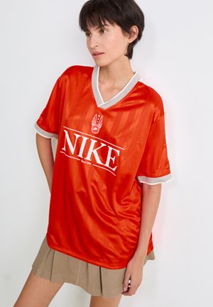 Oranje Nike-tenue met een V-halsontwerp, grijze accenten en wit logo. De stof lijkt glad en glanzend met verticale strepen.